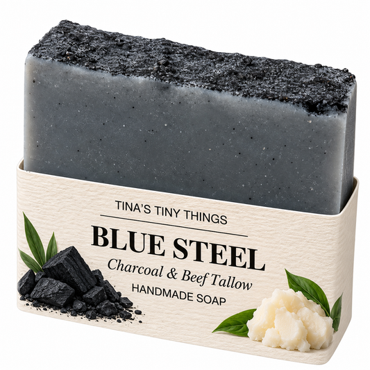 Tina's Tiny Things Blue Steel Handmade Charcoal and Beef Tallow Soap Bar featuring a steel-gray body, rugged charcoal-black textured top, and cream-colored artisan packaging with charcoal and beef tallow illustrations.