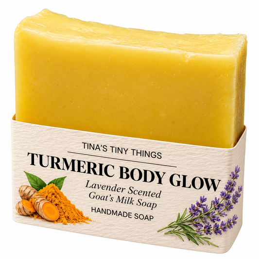Tina's Tiny Things Turmeric Body Glow handmade goat's milk soap bar featuring a vibrant golden-yellow color and cream-colored packaging decorated with turmeric root, golden turmeric powder, and purple lavender flowers.